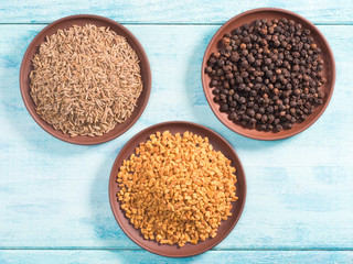 Spice cumin (jeera), black pepper, fenugreek in clay plates on blue wooden background