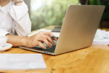 Close up of Young asian woman hand working on laptop while sitting near window in home office.