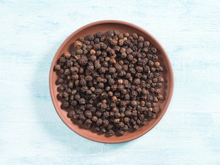 Spice black pepper in clay plate on blue wooden background