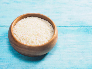 Long grain Basmati rice in wooden bowl on blue wooden background