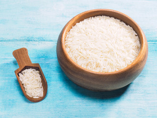 Long grain Basmati rice in wooden bowl and scoop on blue wooden background