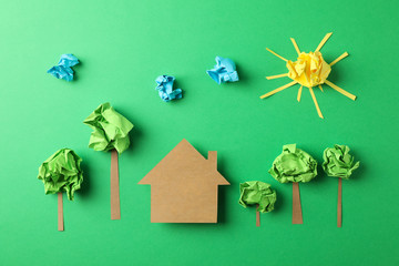 Paper house, clouds, sun and trees on green background, top view