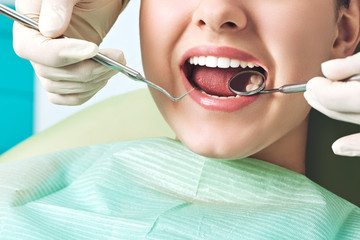 Girl sitting at dental chair with open mouth during oral check up while doctor. Visiting dentist office. Dentistry concept. - obrazy, fototapety, plakaty