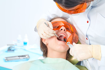 Girl child at the doctor. Dentist places a filling on a tooth with dental polymerization lamp in...