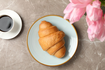 Plate with croissant on grey background with tulips and cup of coffee, top view