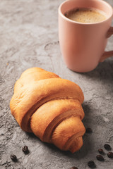 Cup of coffee and croissant on grey background, close up