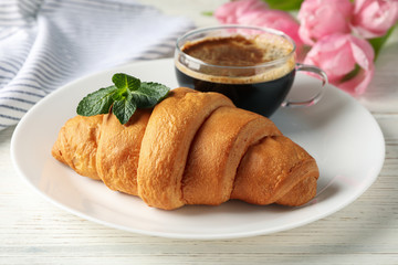 Plate with croissant on wooden background with tulips, close up
