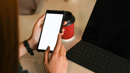 Cropped image of long hair woman holding smartphone in her hands in front a computer tablet next to takeaway coffee cup at the modern working table. Woman lifestyle, Woman relaxation concept.