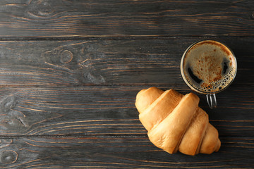 Croissant and cup of coffee on wooden background, top view
