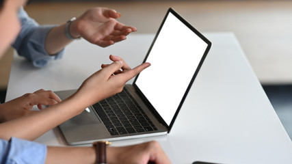 Cropped image of business people discussing/talking about them business result that showing in a laptop at the modern meeting table. Computer laptop with white blank screen for advertise concept.