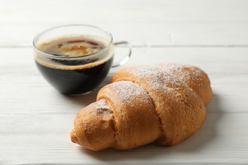 Cup of coffee and croissant on wooden background, close up