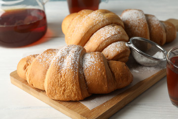 Tasty croissants and cups with tea on wooden background, close up