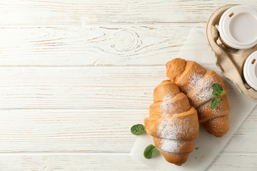Tasty croissants and cups with coffee on wooden background, top view