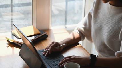 Cropped shot woman holding a stylus pen while using a computer tablet and sitting at the modern...