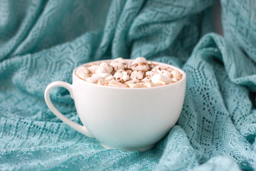 White cup of hot cocoa with marshmallows on blue background.