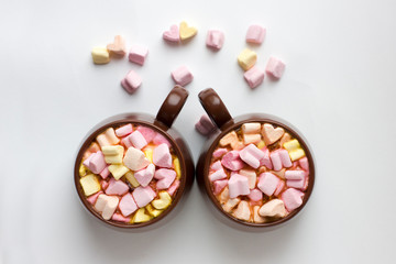 Top view of brown cups of hot cocoa with marshmallows in heart shape on white background.