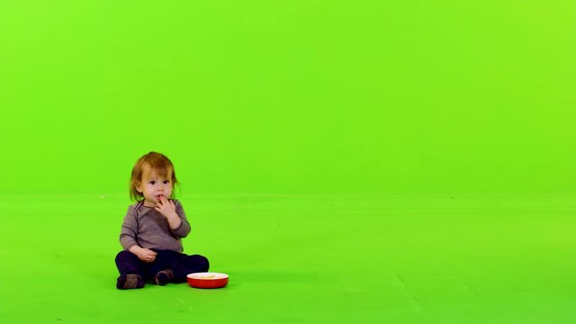 Cute little toddler eating with her hands, full shot over green screen.