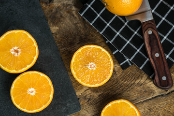 bunch of oranges cut, sliced in half with knife on stone cutting board, old wooden table background