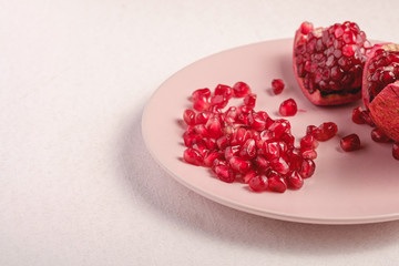 Fresh tasty sweet peeled pomegranate with red seeds in pink plate on white background, angle view,...