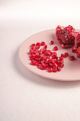Fresh tasty sweet peeled pomegranate with red seeds in pink plate on white background, angle view, healthy food fruits