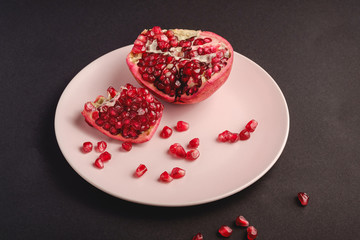 Fototapeta na wymiar Fresh tasty sweet peeled pomegranate with red seeds in pink plate on dark black background, angle view, healthy food fruits