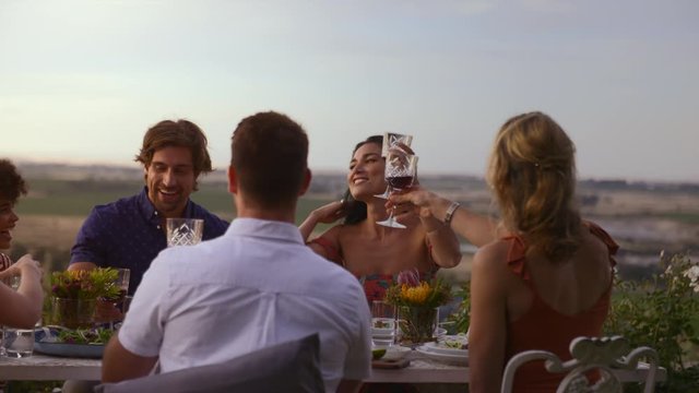 Group of young friends having fun at a dinner party, raising a celebratory toast with wine. Millennials celebrating a special occasion with wine.