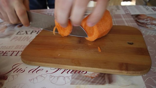 Male hand cuts carrots on a cutting board on the table. 