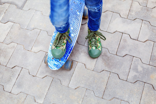 Close-up Of A Girl's Legs In Sneakers Standing On A Blue Skate. Hipster Girl On A Skateboard. Street Style.