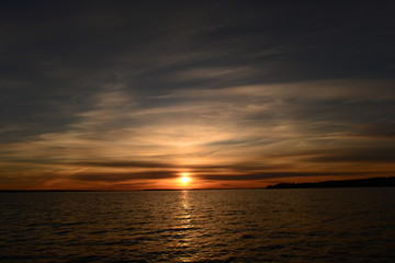 Spring bright sun glowing at sunset in the clouds of blue sky on the horizon above the lake water