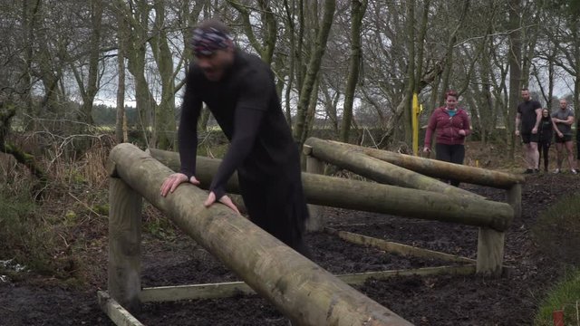 Group of people participating in a Tough Mudder mud run / assault / obstacle course. Jumping over wooden beams - Stock 4K Video clip footage