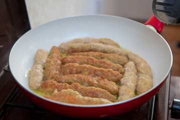 The long cutlet is fried in a red pan. She cooks the cutlet in a white pan.