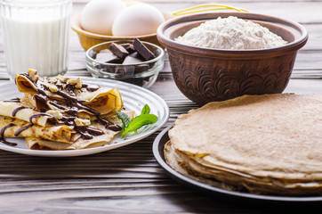 French crepes with chocolate sauce walnuts eggs and flour on wooden kitchen table
