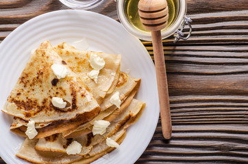 Flat lay of French crepes with butter and honey in ceramic dish on wooden kitchen table