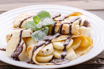 French crepes with chocolate sauce and banana in ceramic dish on wooden kitchen table