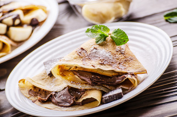 French crepes with chocolate sauce and banana in ceramic dish on wooden kitchen table
