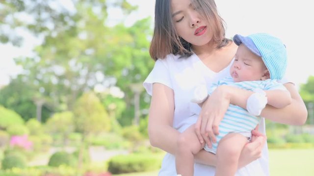 Slow motion of a asian mother smiling with her 3 months old baby boy on green grass outdoor in park. - Powered by Adobe