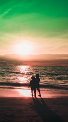 Fototapeta premium Dramatic sky and clouds on the beach at sunset. Silhouette of two children watching the sunset on the beach. City residents are enjoying a weekend by the sea. 