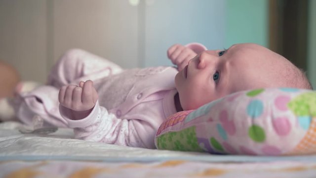 Newborn baby girl. A newborn baby lies on the bed on an orthopedic pillow. The girl looks away.