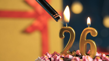 Birthday cake number 26 golden candles burning by lighter, background gift yellow box tied up with...