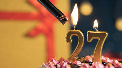 Birthday cake number 27 golden candles burning by lighter, background gift yellow box tied up with red ribbon. Close-up