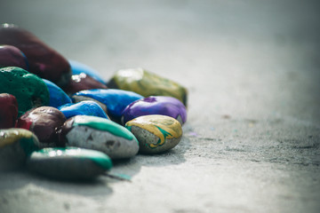 Many small pebbles covered with multicolored paint lie on surface