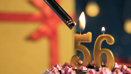 Birthday cake number 56 golden candles burning by lighter, background gift yellow box tied up with red ribbon. Close-up
