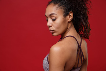 Side view of attractive young african american sports fitness woman in sportswear posing working out isolated on red wall background in studio. Sport exercise healthy lifestyle concept. Looking down.