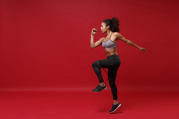 Fototapeta na wymiar Side view of young african american sports fitness woman in sportswear working out isolated on red background in studio. Sport exercises healthy lifestyle concept. Doing exercises with elastic band.