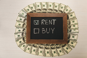 top view of chalkboard with rent and buy lettering near dollar banknotes on desk