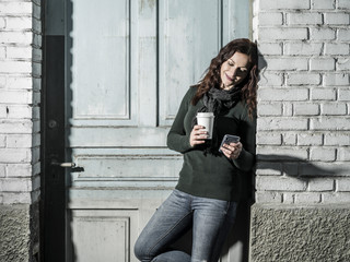 Woman checking her messages and drinking coffee outside