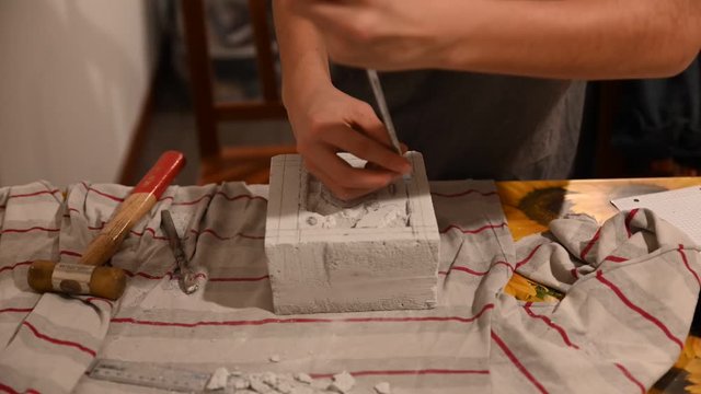 Time lapse footage, the gray block of lightened concrete is carved with a screwdriver and hammer by a young Caucasian boy. Draw a nest for ants.