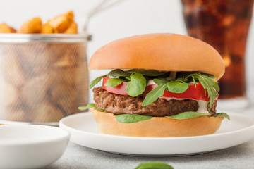 Healthy vegetarian meat free burger on round ceramic plate with vegetables on light table background with potato wedges and glass of cola.