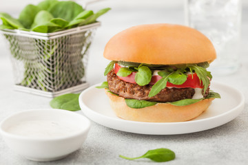 Healthy vegetarian meat free burger on round ceramic plate with vegetables and spinach on light table background.