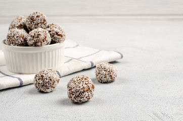 Energy balls of dates, nuts, oats, sprinkled with coconut powder closeup in a white plate on a...